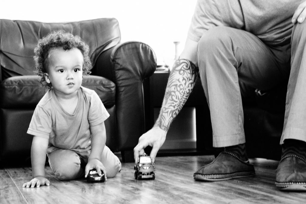 A black and white photo of A dad and his son playing cars on the floor, Highland Park, CA