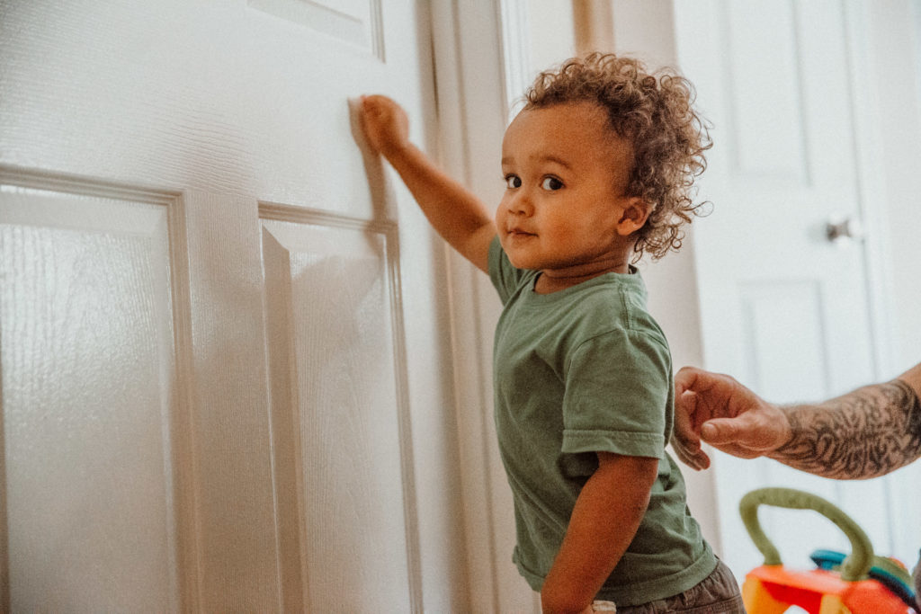 A toddler knocks on a door with his dad behind him, Highland Park, Los Angeles, CA