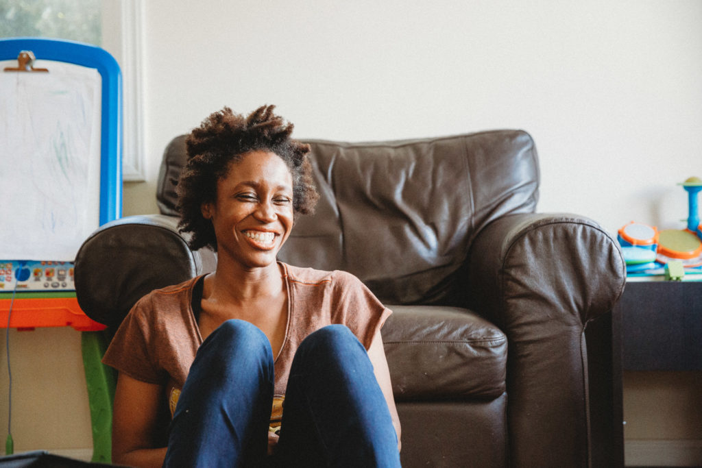 A woman smiling and leaning against a chair in living room