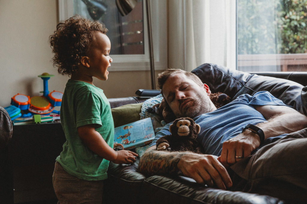 Toddler talking to dad asleep on the couch