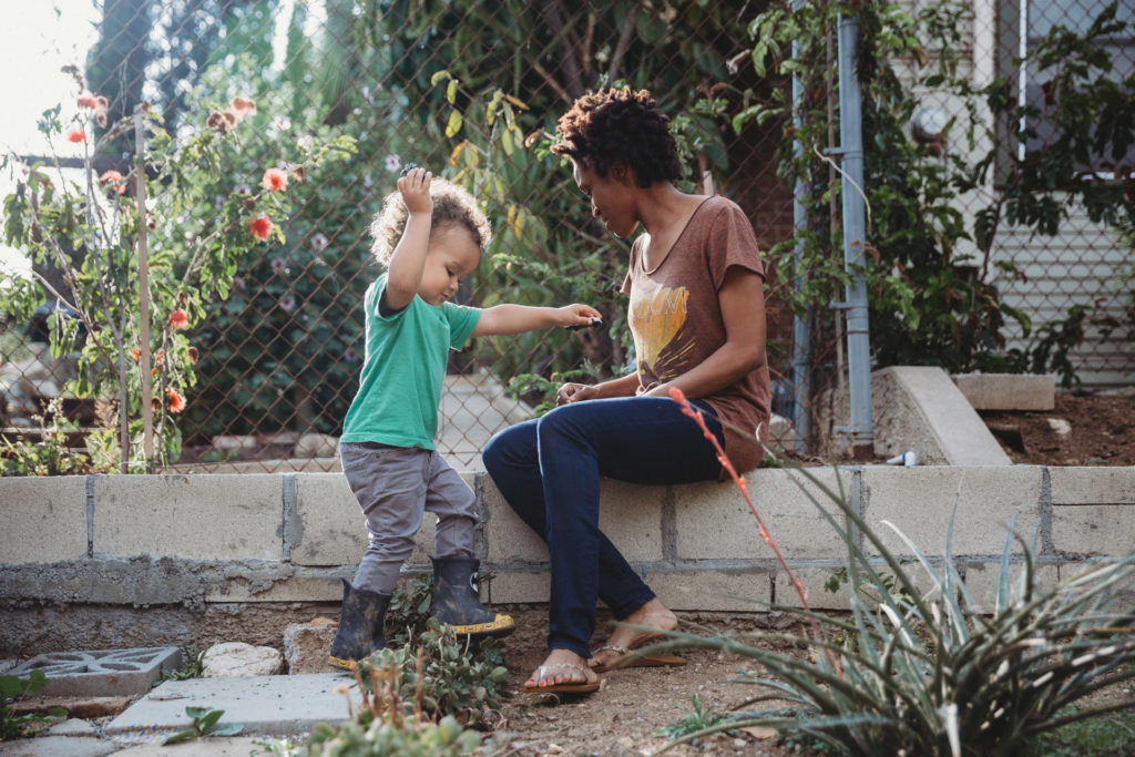 Toddler in rainboots hanging outside with mom