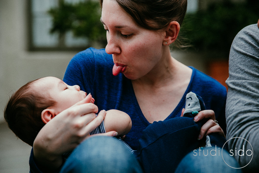 Mom sticking her tongue out at baby in her arms, Los Angeles, CA