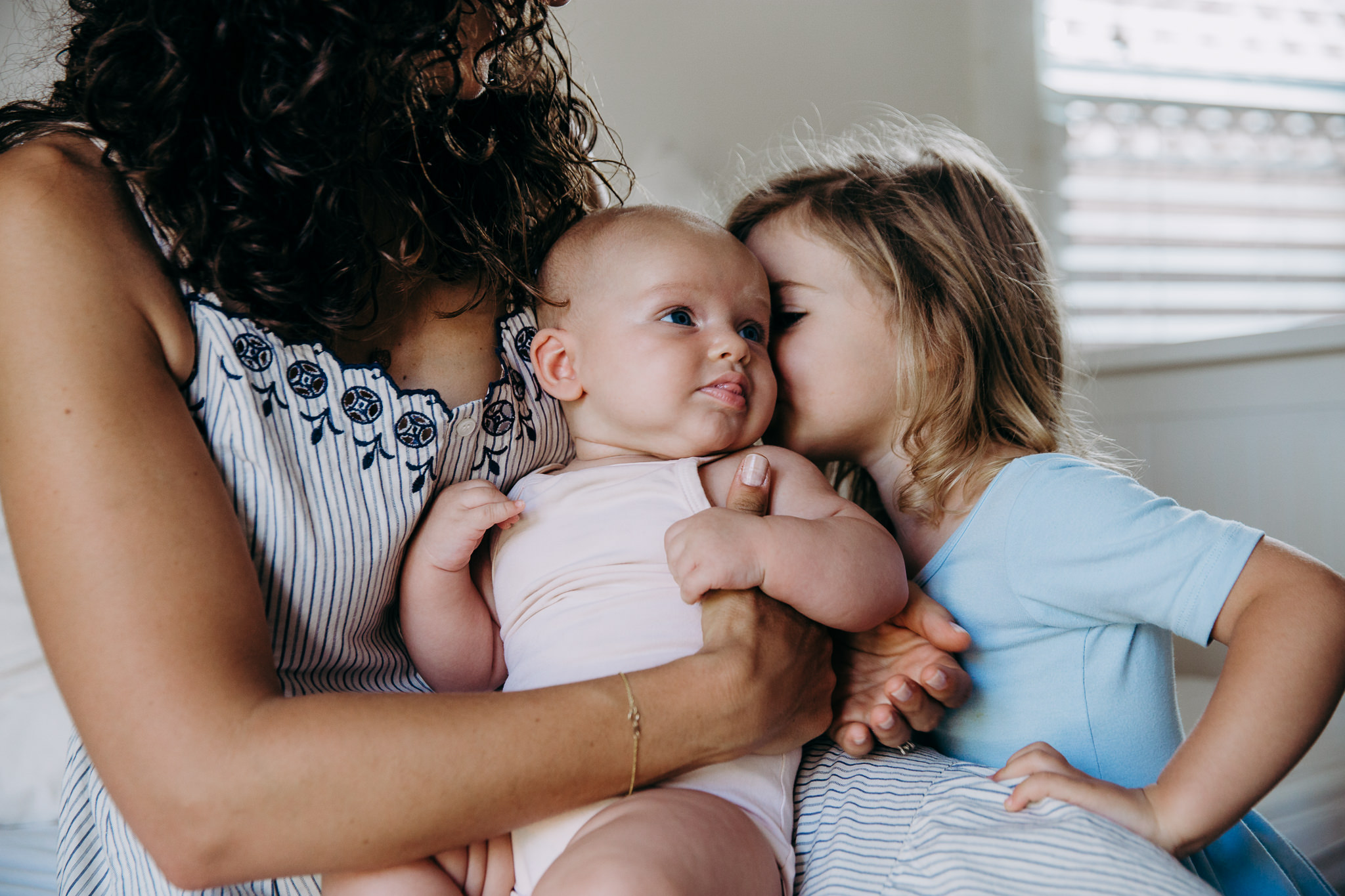 Mama holding baby while older sister whispers into her ear in Atwater Village, CA