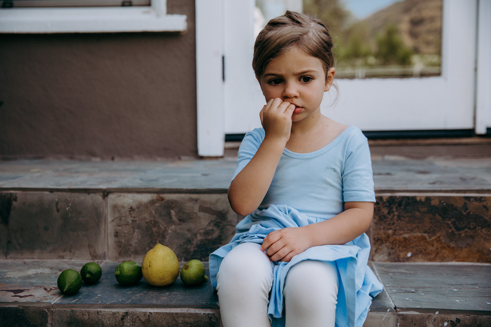 little girl sits alone on a step with lemons and limes next to her - Atwater Village, CA