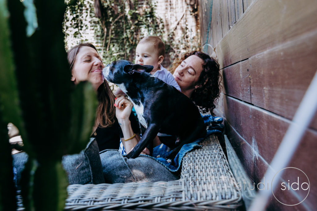 Young family outside, dog kisses one of the mama's faces