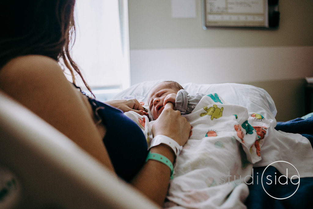 Newborn baby holds mom's finger while lying in her lap