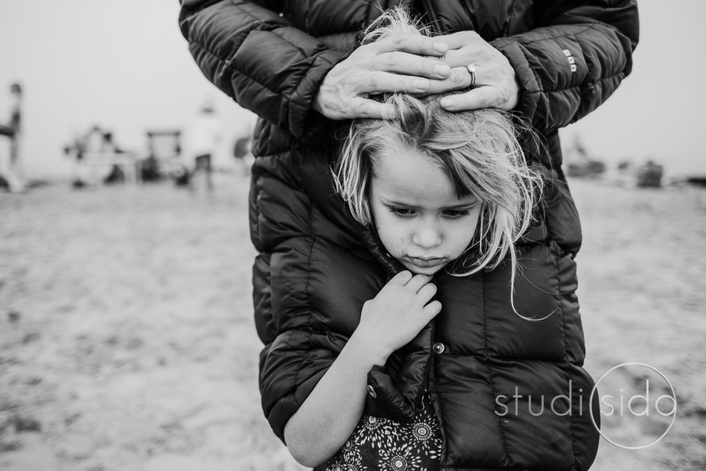 A girl cuddles in her mom's coat on the beach in Santa Monica, California.