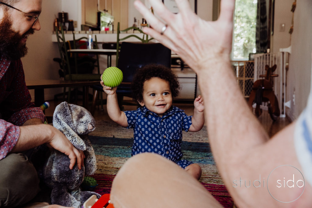 Two dads sit on the floor and play with their son with a ball and a toy bunny in West Hollywoood, CA.