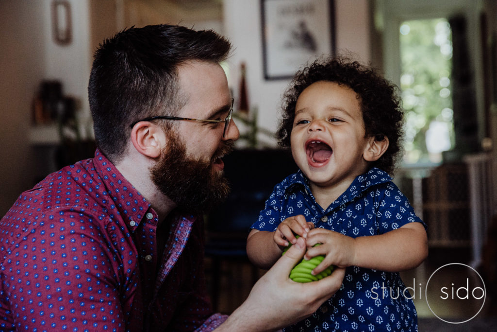 A little boy laughs with his dad and holds a ball in West Hollywood, CA.