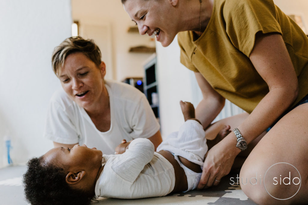 Two mamas smile and laugh with their baby in their home in Silver Lake, Los Angeles