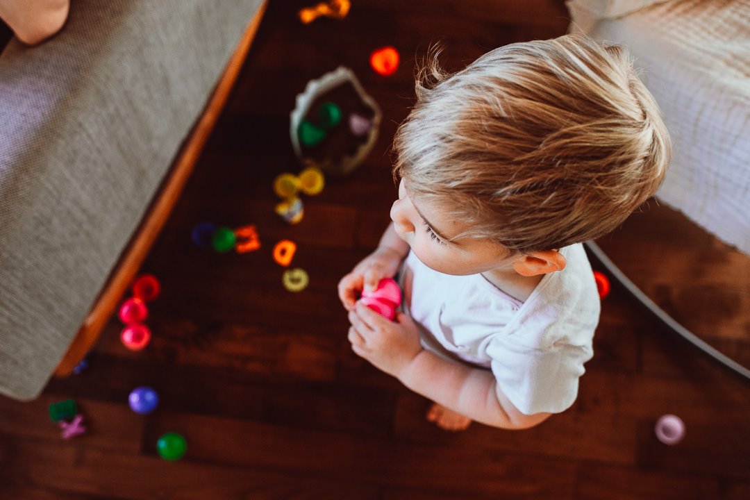 Toddler Standing in Living Room Surrounded by Colorful Toys