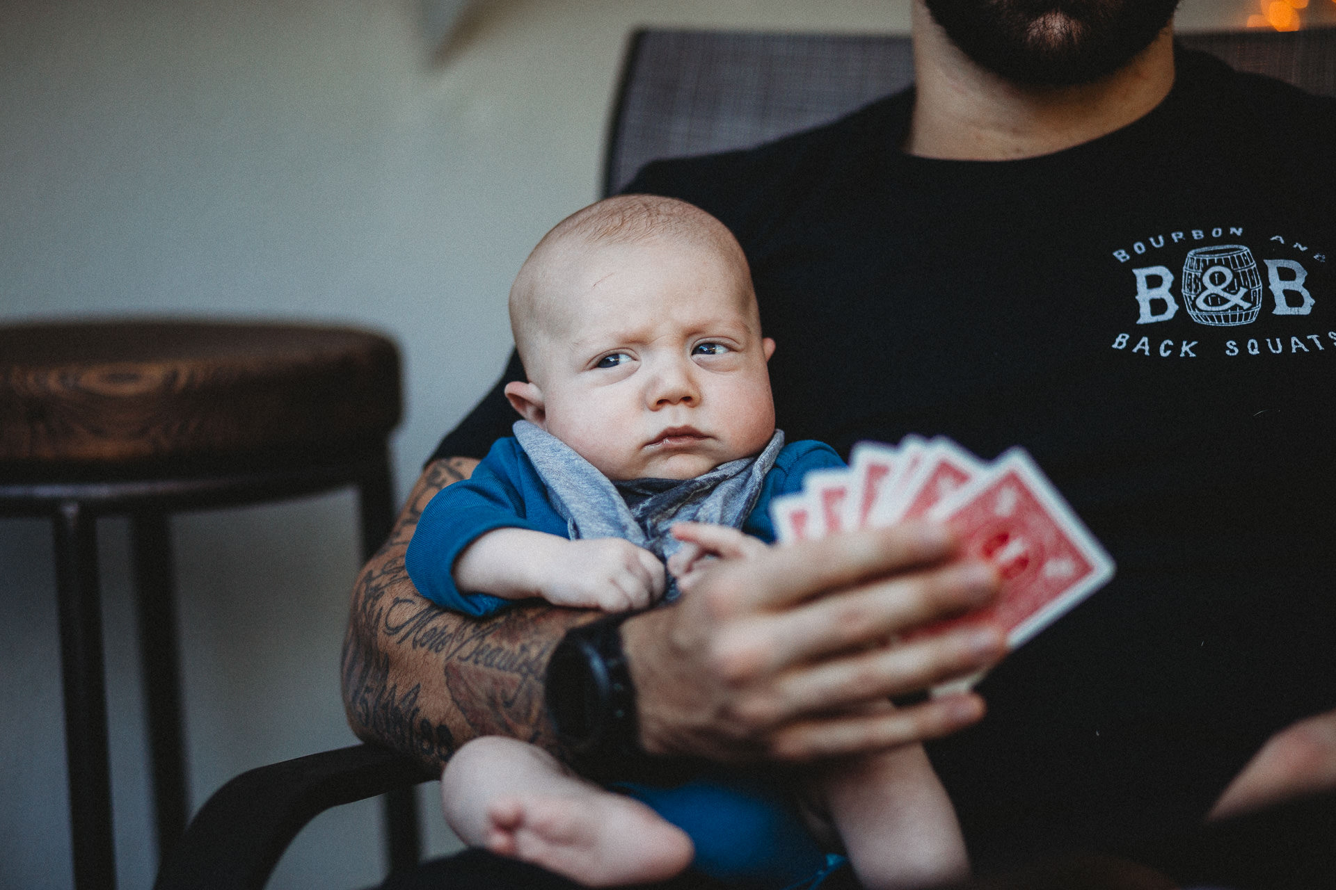 Baby looks serious in dad's lap during a card game in Los Angeles, CA