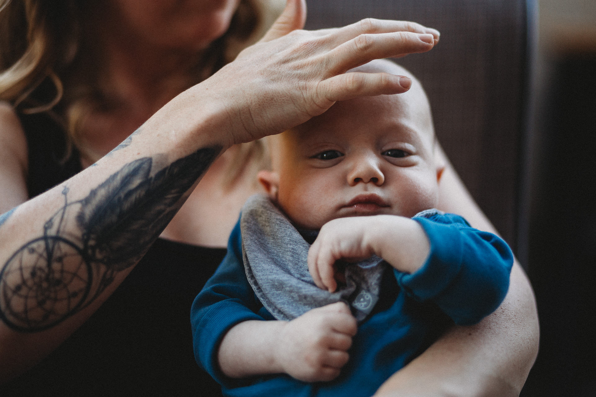 A mom with tattoos gently touches her baby's head