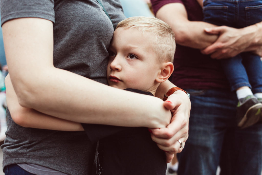 Boy hugs his mom while his younger brother is held by his dad at Disneyland, Anaheim, CA