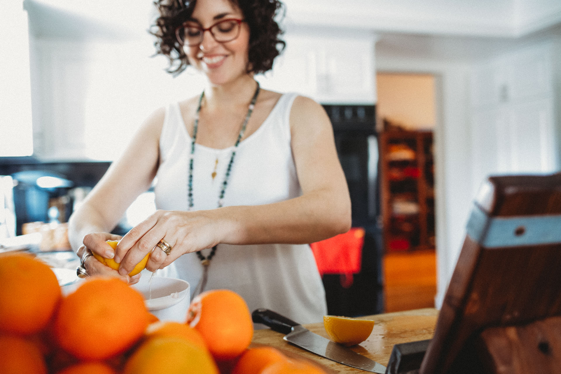 Woman Squeezing Oranges Into Bowl In Kitchen