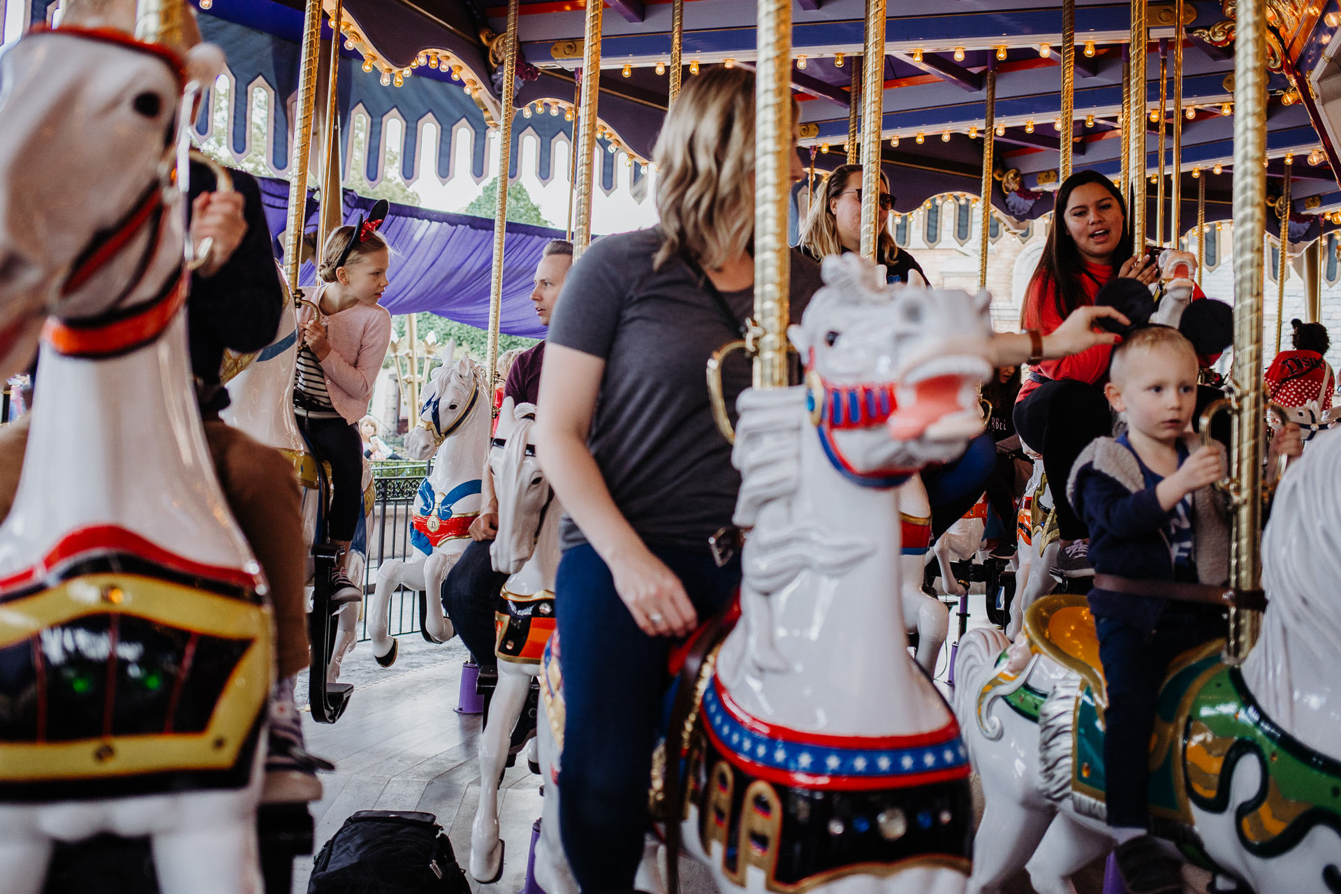 A family rides the carousel, mom and boys in front, dad and daughter in the back, at Disneyland