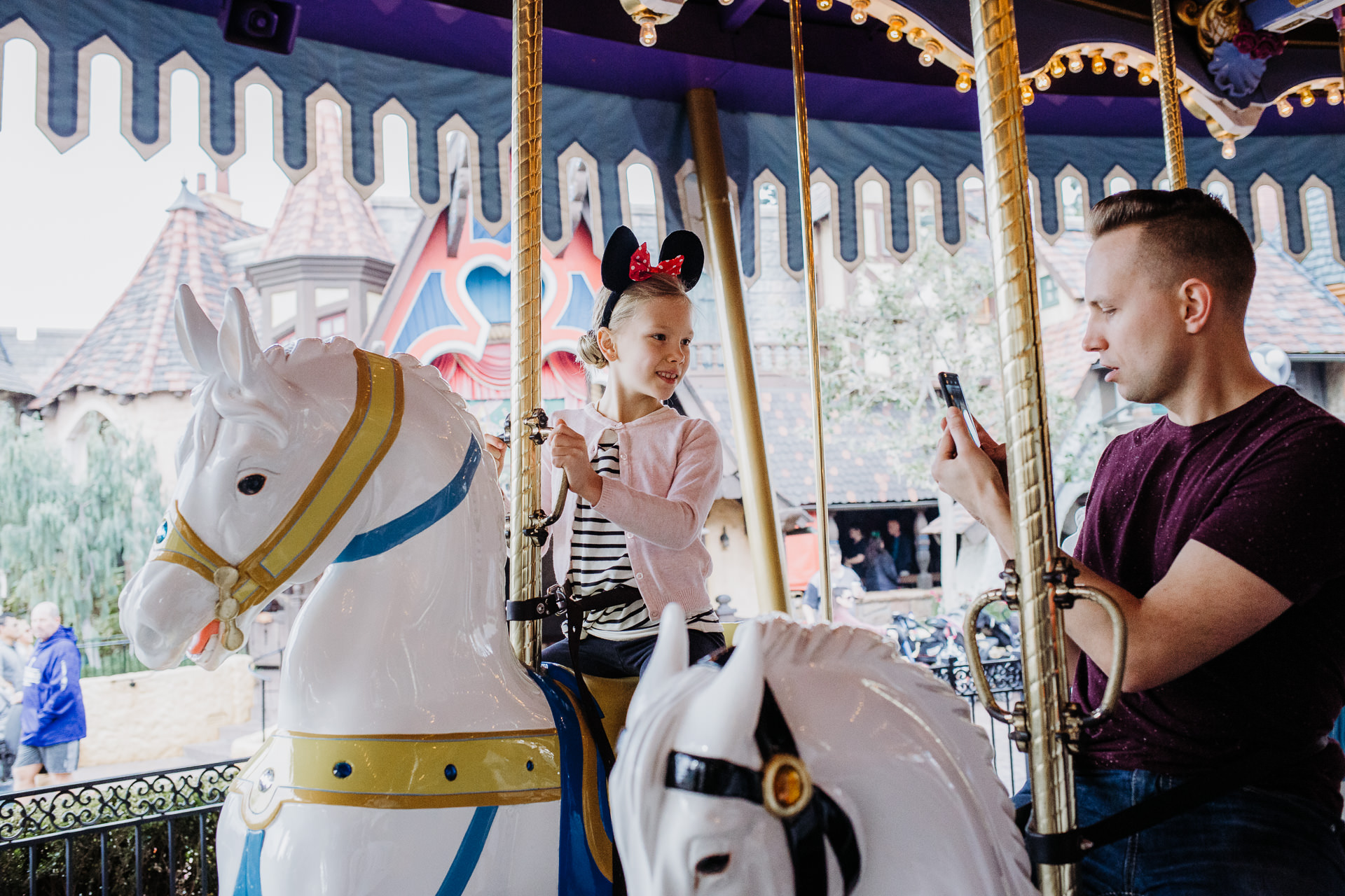 A dad takes a cell phone photo of his daughter on the carousel at Disneyland