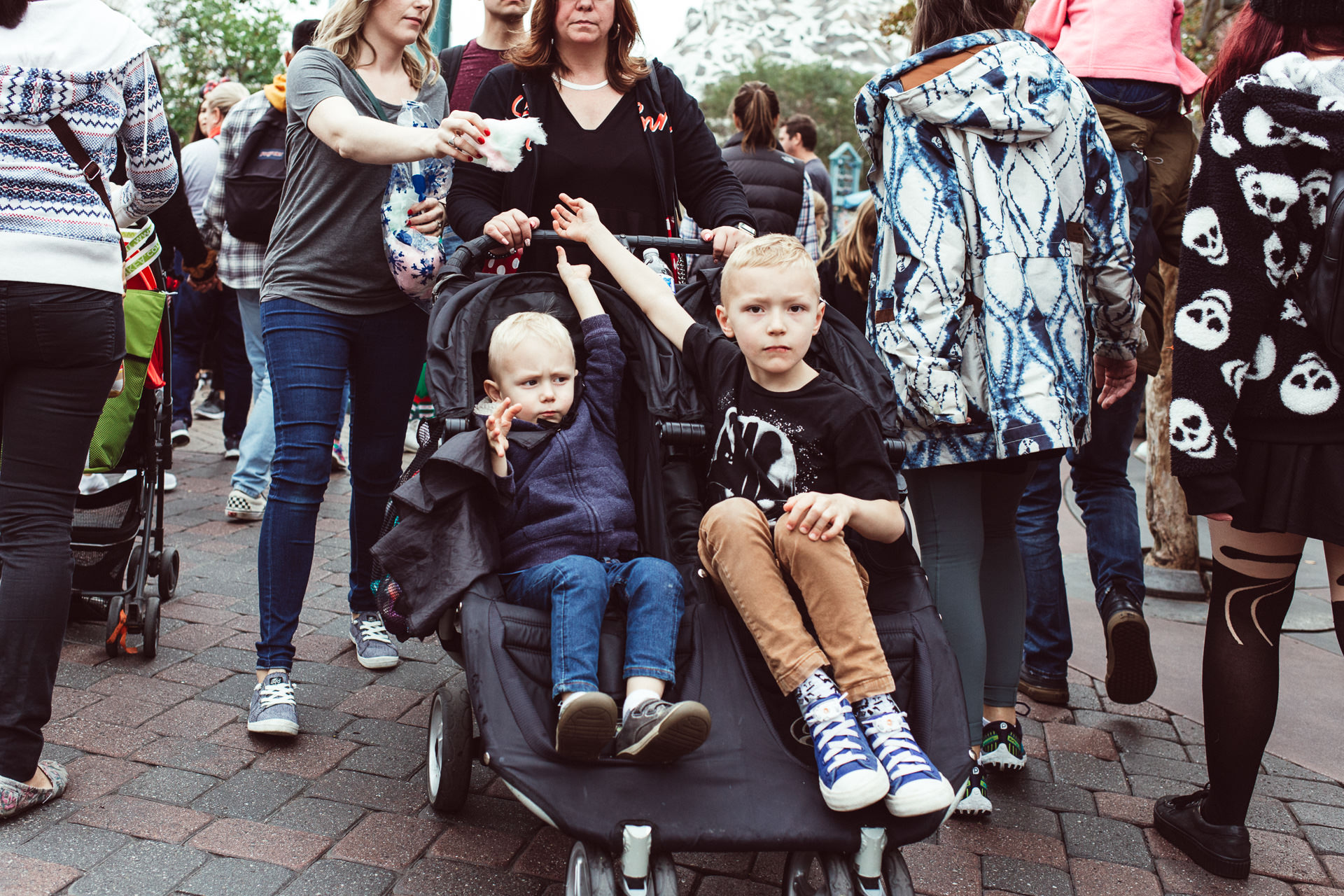 Boys in stroller reach for cotton candy from their mom at Disneyland