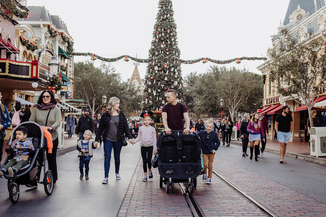 A family walks down Disneyland's Main Street with the Christmas tree behind them