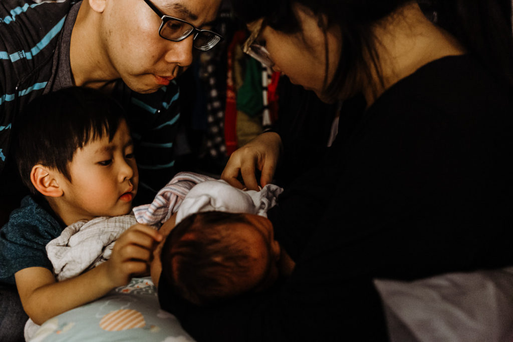 A baby nurses while dad and brother look on.