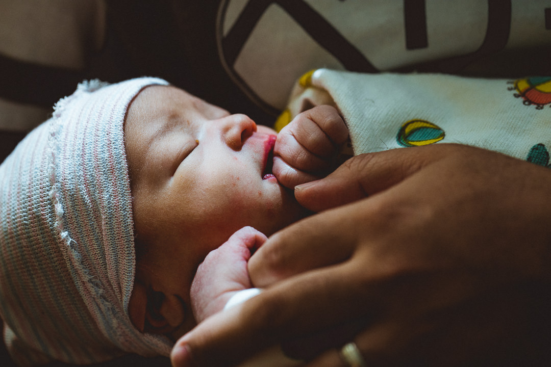 A sleeping newborn baby holding his father's finger