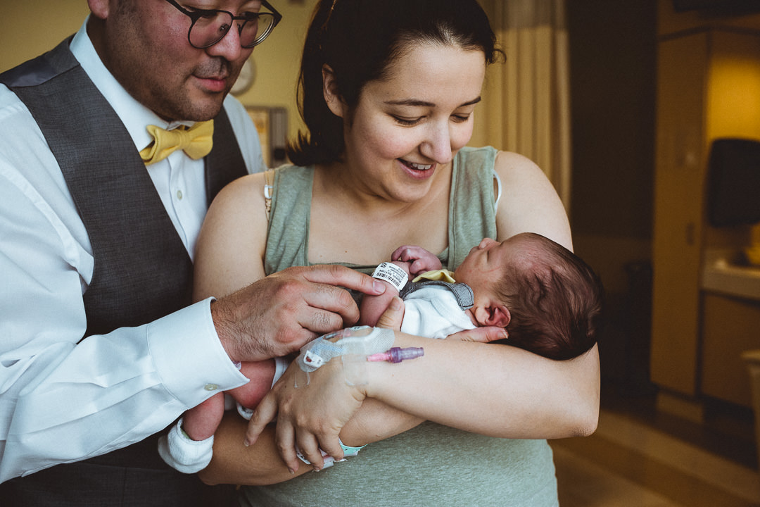 Mom and Dad Snuggling Newborn In Hospital