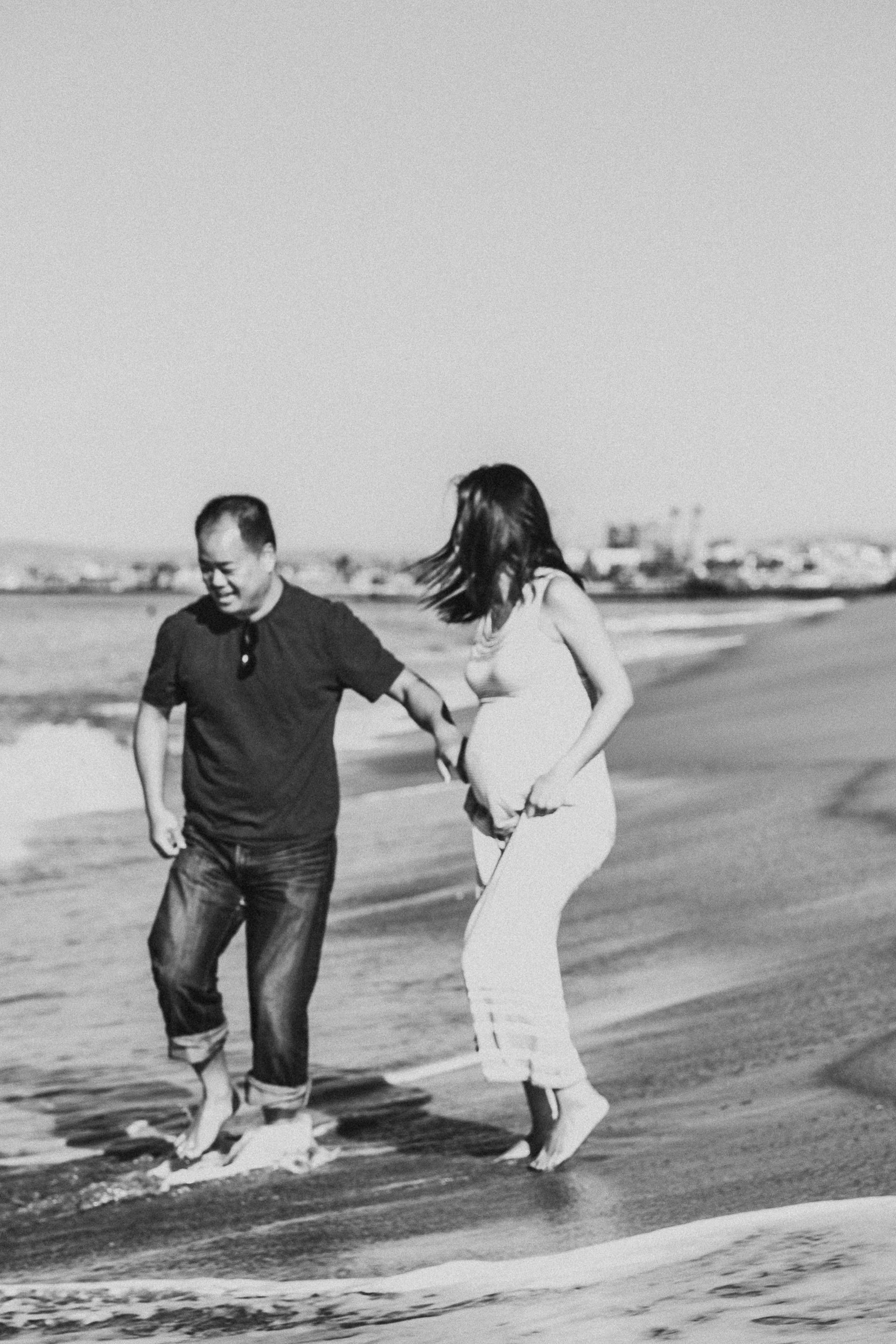 Pregnant woman and husband play in the waves in California