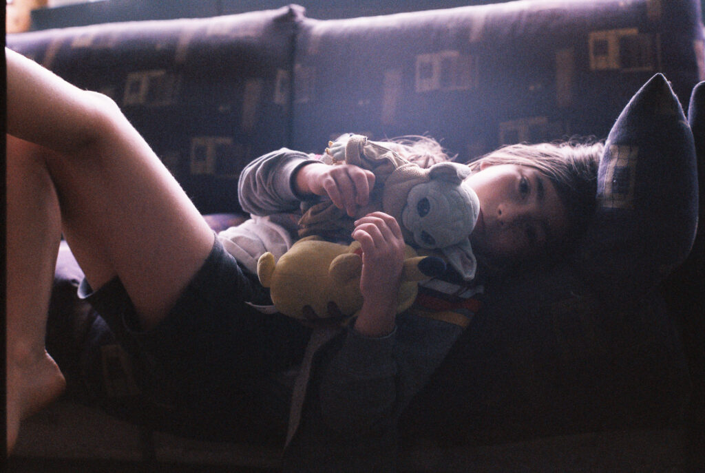 a boy lying on a couch, holding a baby Yoda stuffed animal