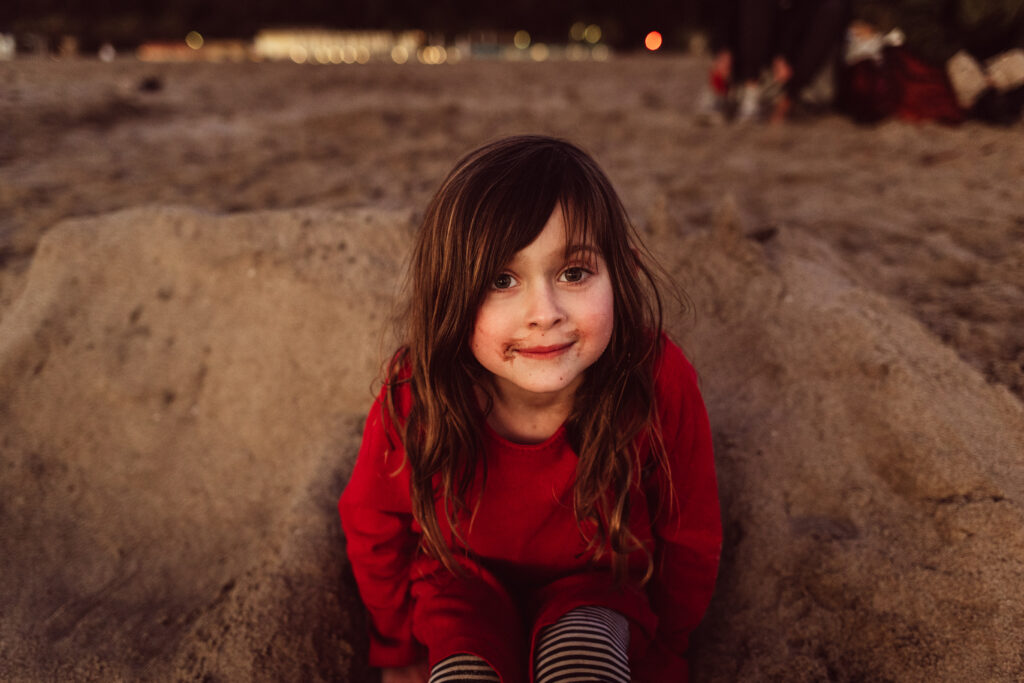 A young girl looks at the camera while sitting in the sand on Santa Monica Beach,, CA