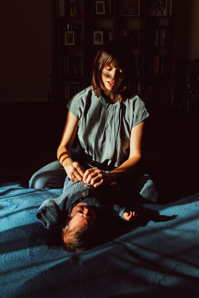 A mother dresses her newborn with beautiful light coming in the window