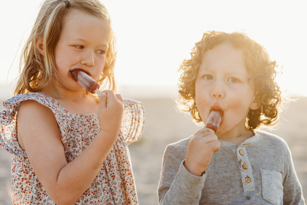 kids eat popsicles on a southern California beach at sunset