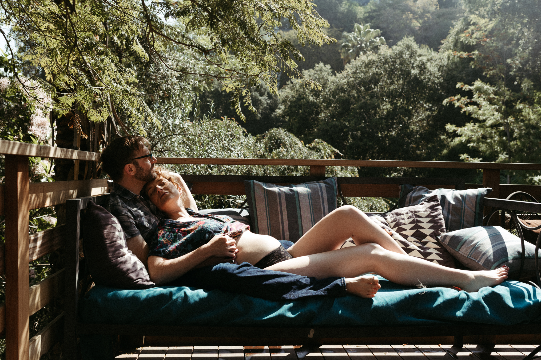 Pregnant woman lies in her partner's arms on their deck in Echo Park, Los Angeles, CA