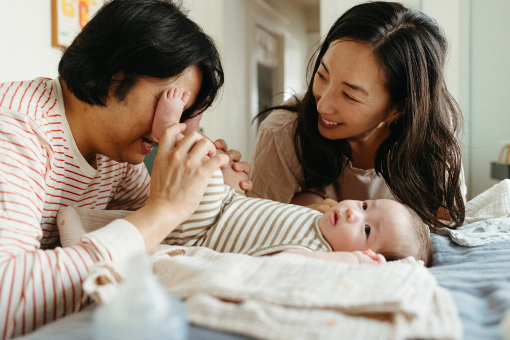 Dad plays peekaboo with baby's feet while mom laughs