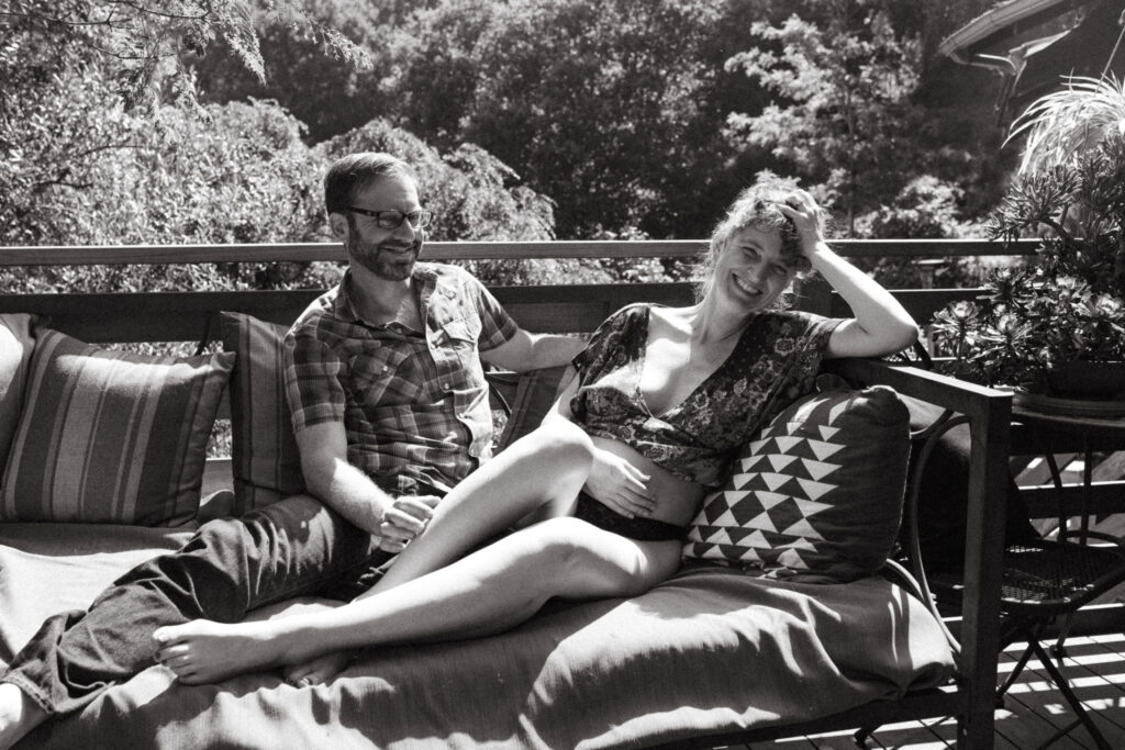 Pregnant Mom and Dad Snuggled Up on Couch Outdoors Black and White Photo