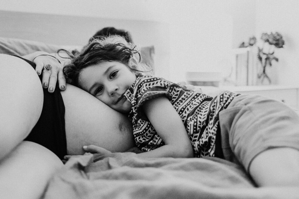 Young Child Snuggles Up On Pregnant Moms Belly Black and White Photos