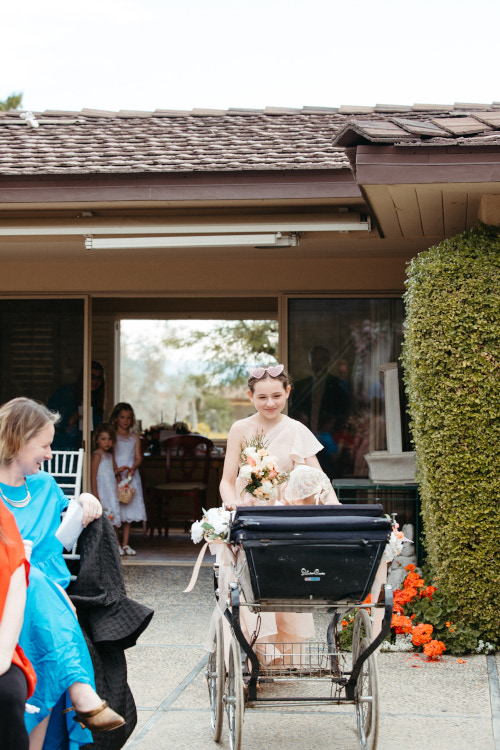 Girl pushing antique carriage with baby inside down wedding aisle